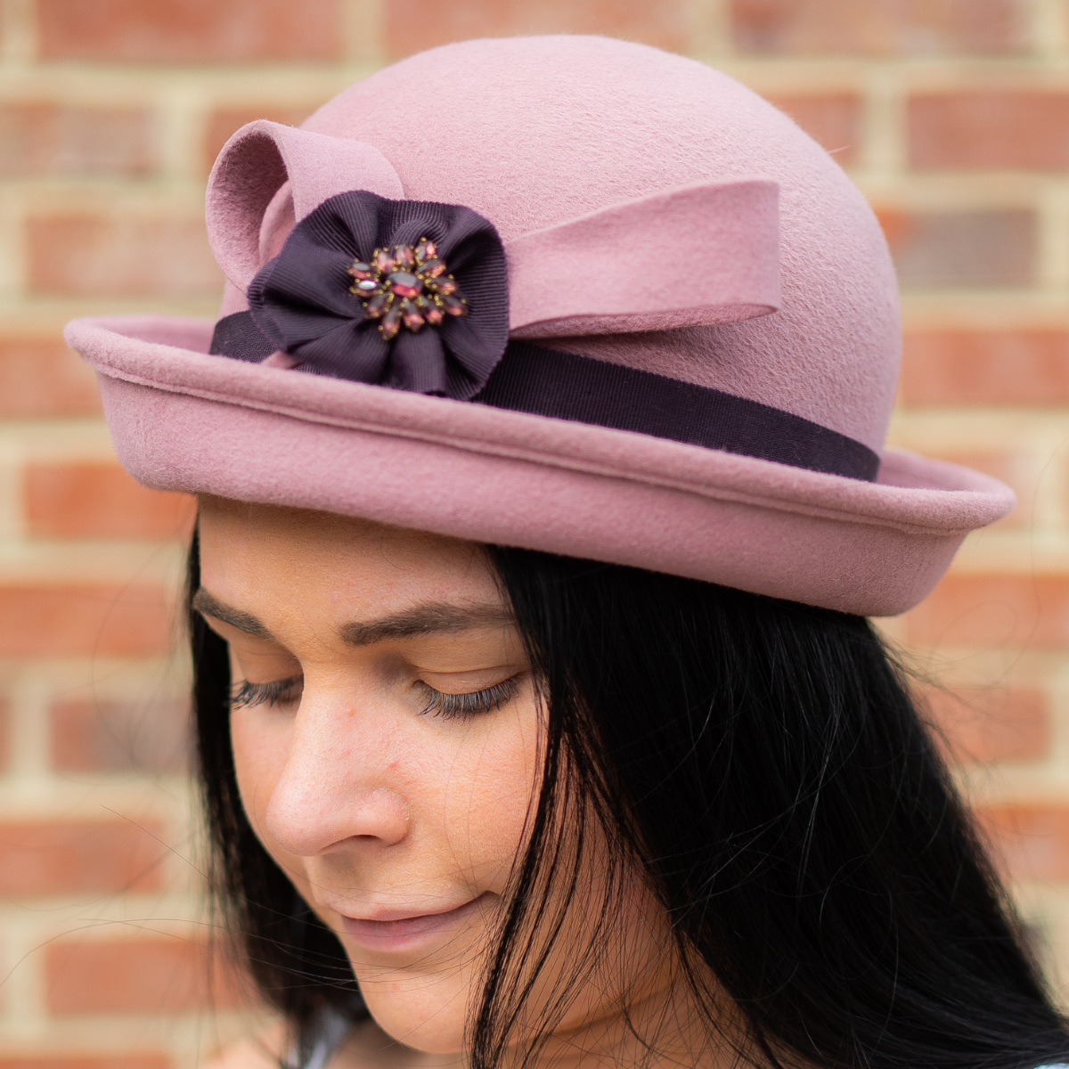 Lady wearing a bowler hat, hand decorated with ribbon and a brooch.