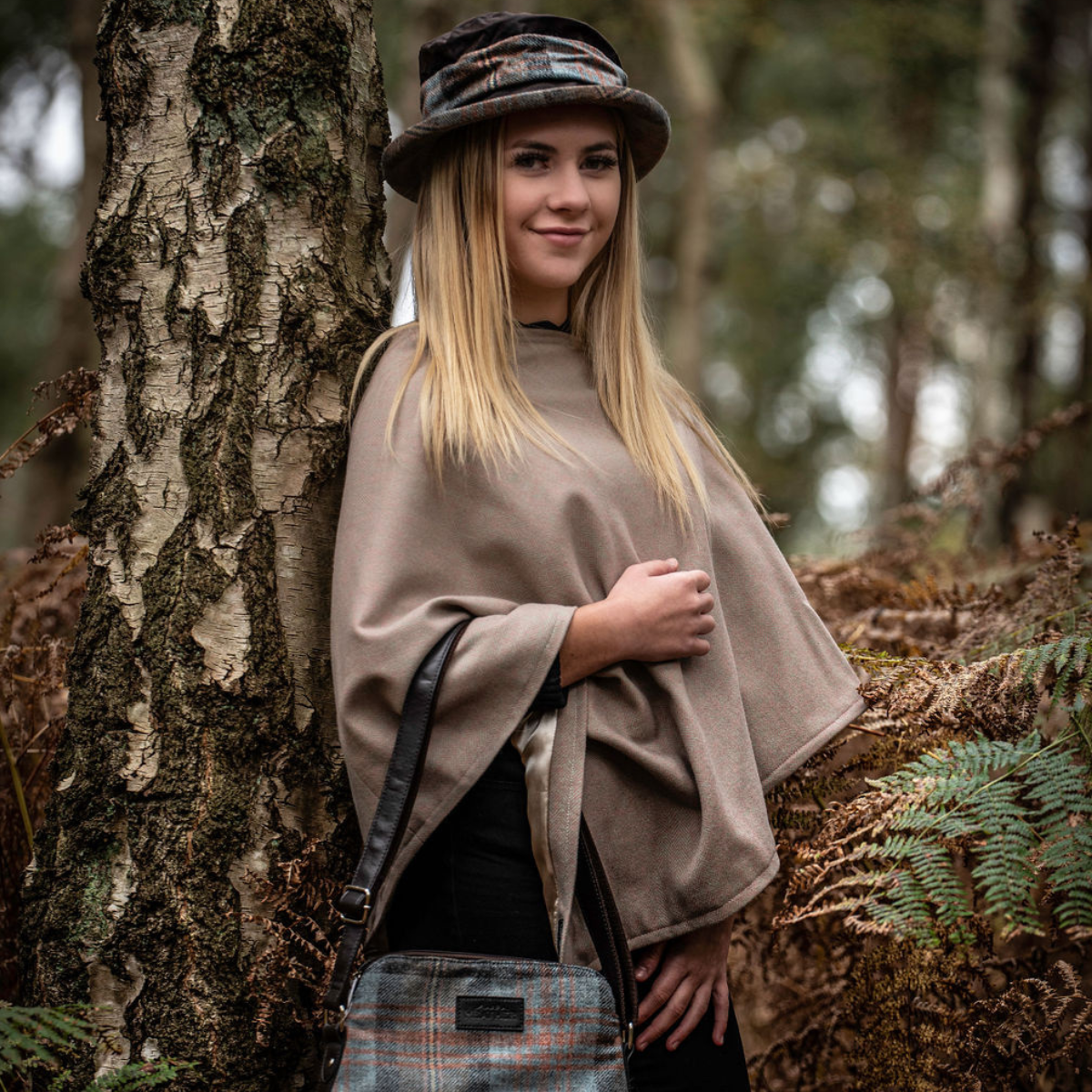 Lady leaning against a tree wearing a beige coloured poncho